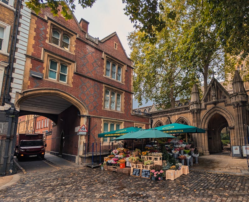 A street scene in Bankside featuring a flower stall set up under a teal umbrella with the website 'floweronwellington.co.uk' printed on it. The stall displays a variety of fresh flowers, including ros