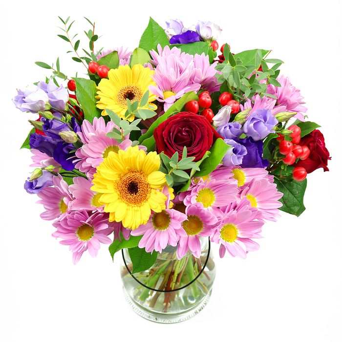 In this image, a generously sized mixed bouquet rises confidently from a cylindrical clear glass vase, set against a plain white background that highlights every colour and texture as clearly as a gallery wall along Bankside. The arrangement feels both abundant and composed: at the centre, rich, deep red roses unfurl in tight spirals, their velvety petals giving a sense of depth and timeless affection. Nearby, bright yellow gerbera daisies with dark, warm brown centres beam outward, offering a cheerful, almost sunlit quality that recalls a walk along the Thames on a clear day. Surrounding these focal blooms, soft pink daisy-style chrysanthemums spread outward in layers, their many slender petals and small yellow eyes creating a soothing cushion of pastel colour. Threaded between these pinks are graceful stems of purple and lavender lisianthus, their slightly ruffled, bell-shaped flowers introducing cool tones and a sophisticated, modern note. Scattered among the blossoms, plump red hypericum berries gleam with a polished finish, adding playful dimension and catching the light like tiny ornaments. Lush greenery in several shades of green-broad, dark leaves that anchor the design and lighter, more delicate sprigs that soften its edges-wraps around the flowers, giving the bouquet a natural, garden-fresh silhouette. Through the transparent vase, you can see the neatly cut stems resting in clear water, a quiet testament to professional floristry and freshness. The overall impression is one of joyful celebration with a refined edge, perfectly suited to congratulate a new opening near Blackfriars Bridge, thank a host in a Bankside apartment, or brighten a creative studio close to Tate Modern.